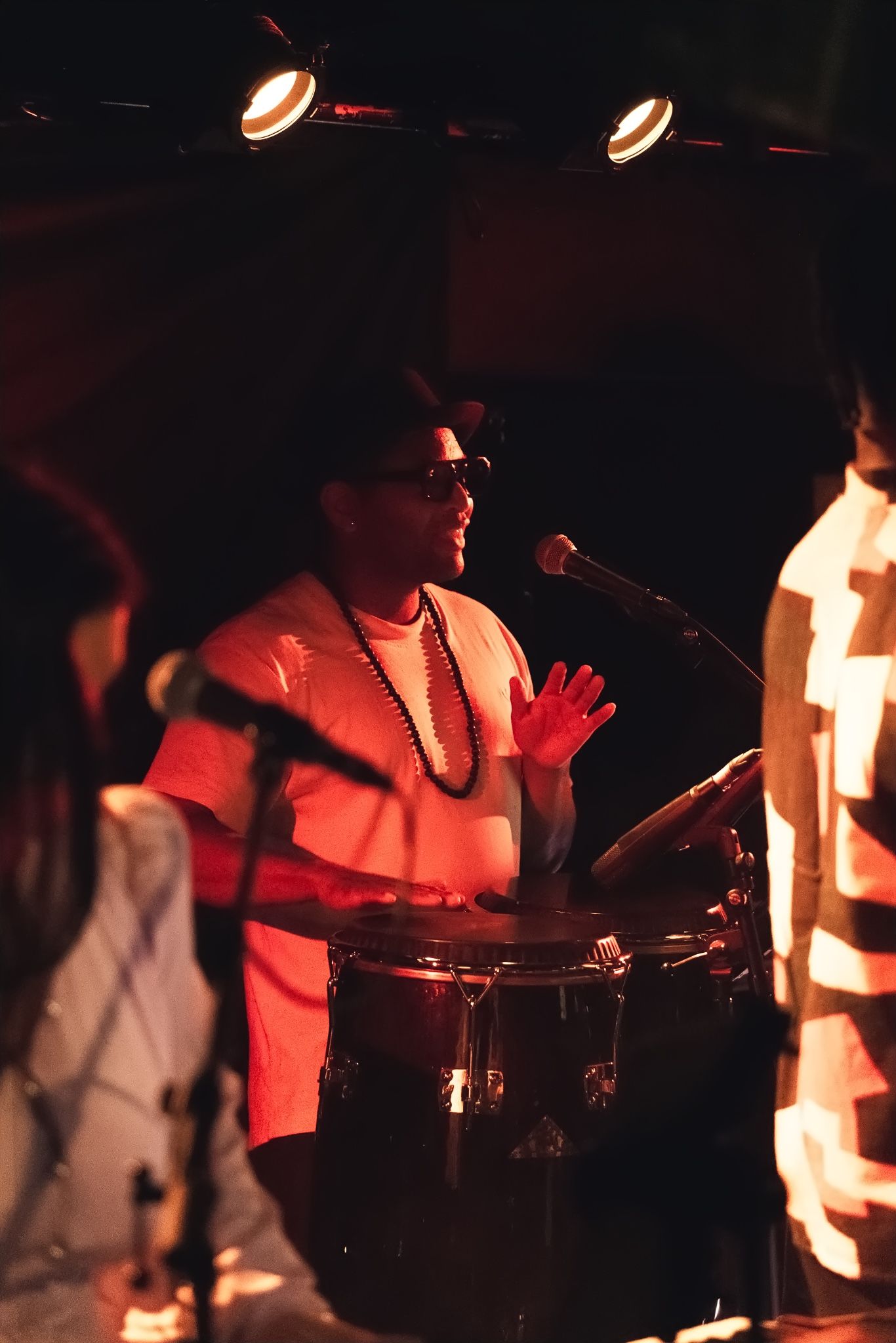 A percussionist in sunglasses singing into a microphone while playing a drum.