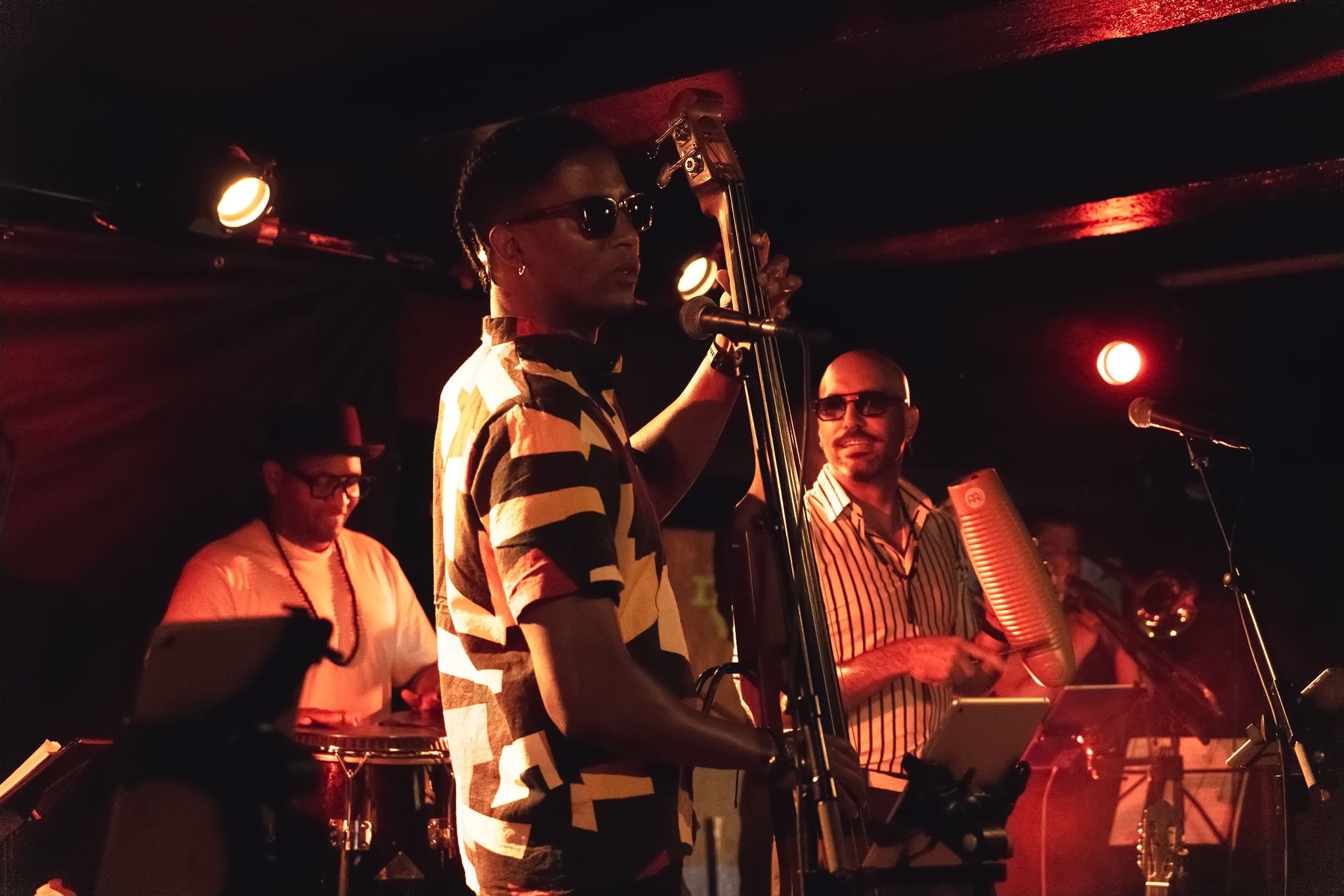 A double bassist and a percussionist laughing together on stage in red light.