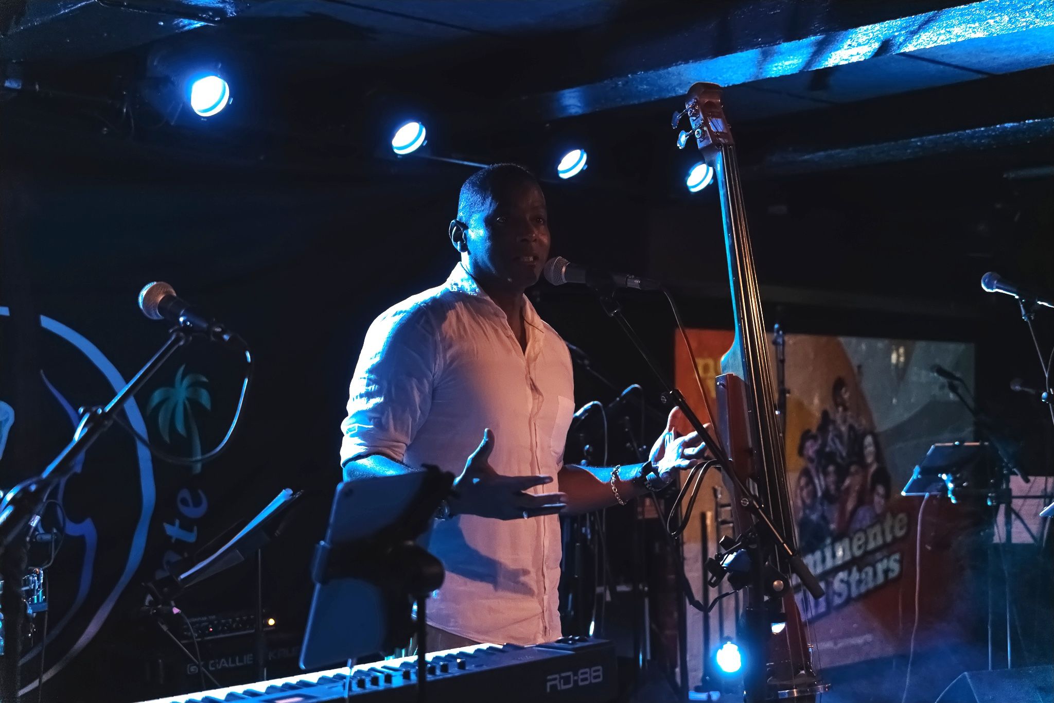 A singer in a white shirt at the microphone, double bass and band banner behind him.