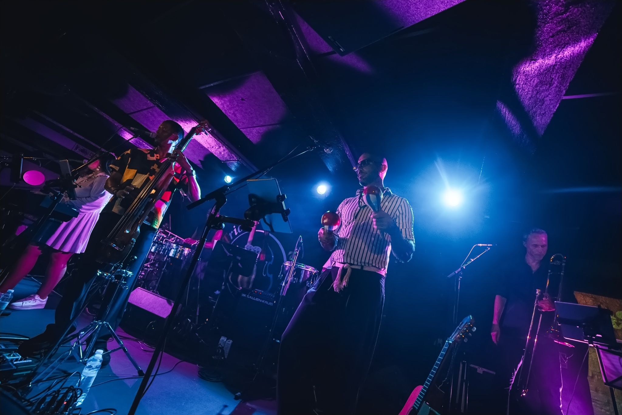 The stage from a low angle in blue and violet light, horns and percussion in view.