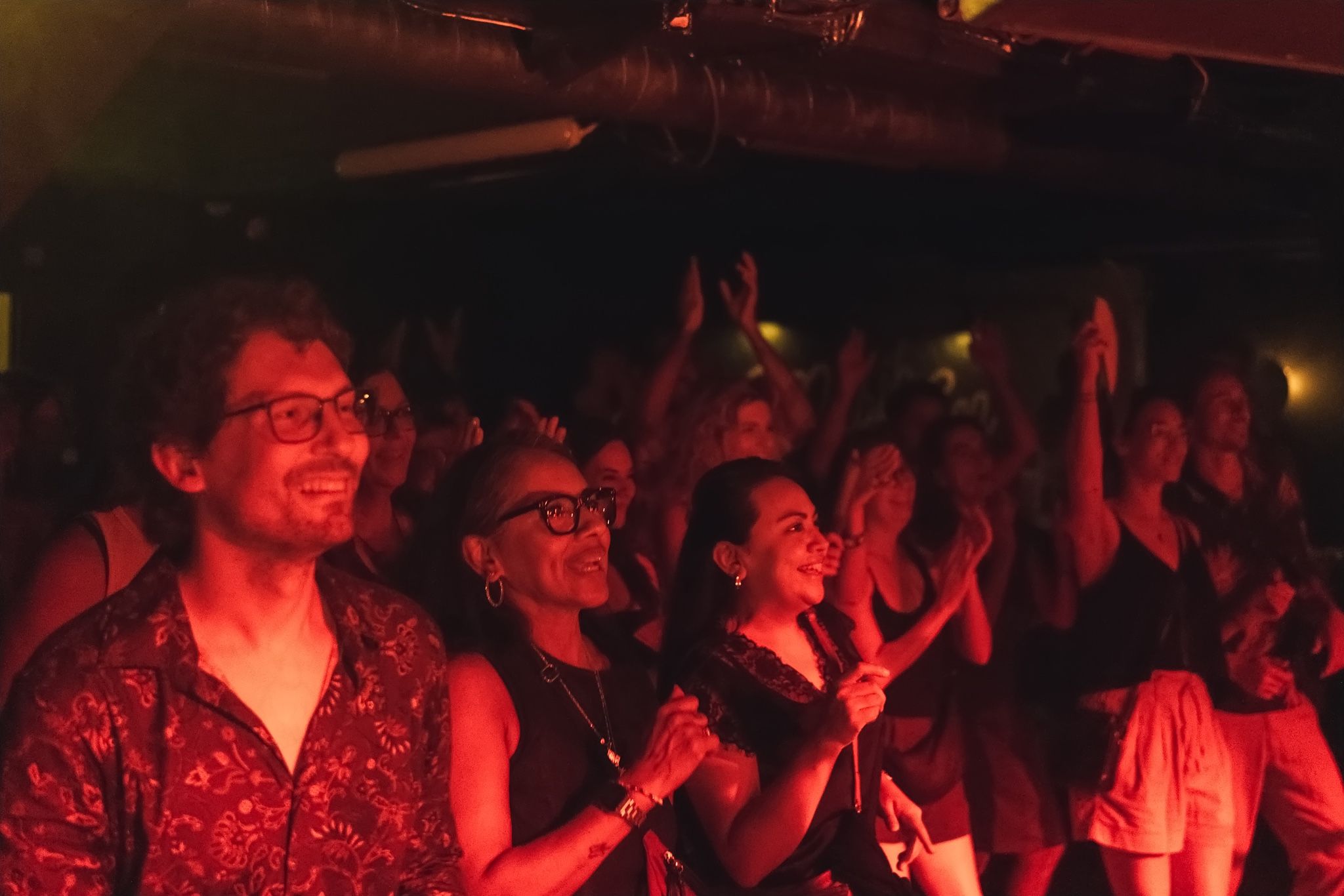 People in the audience smiling and clapping in red light.